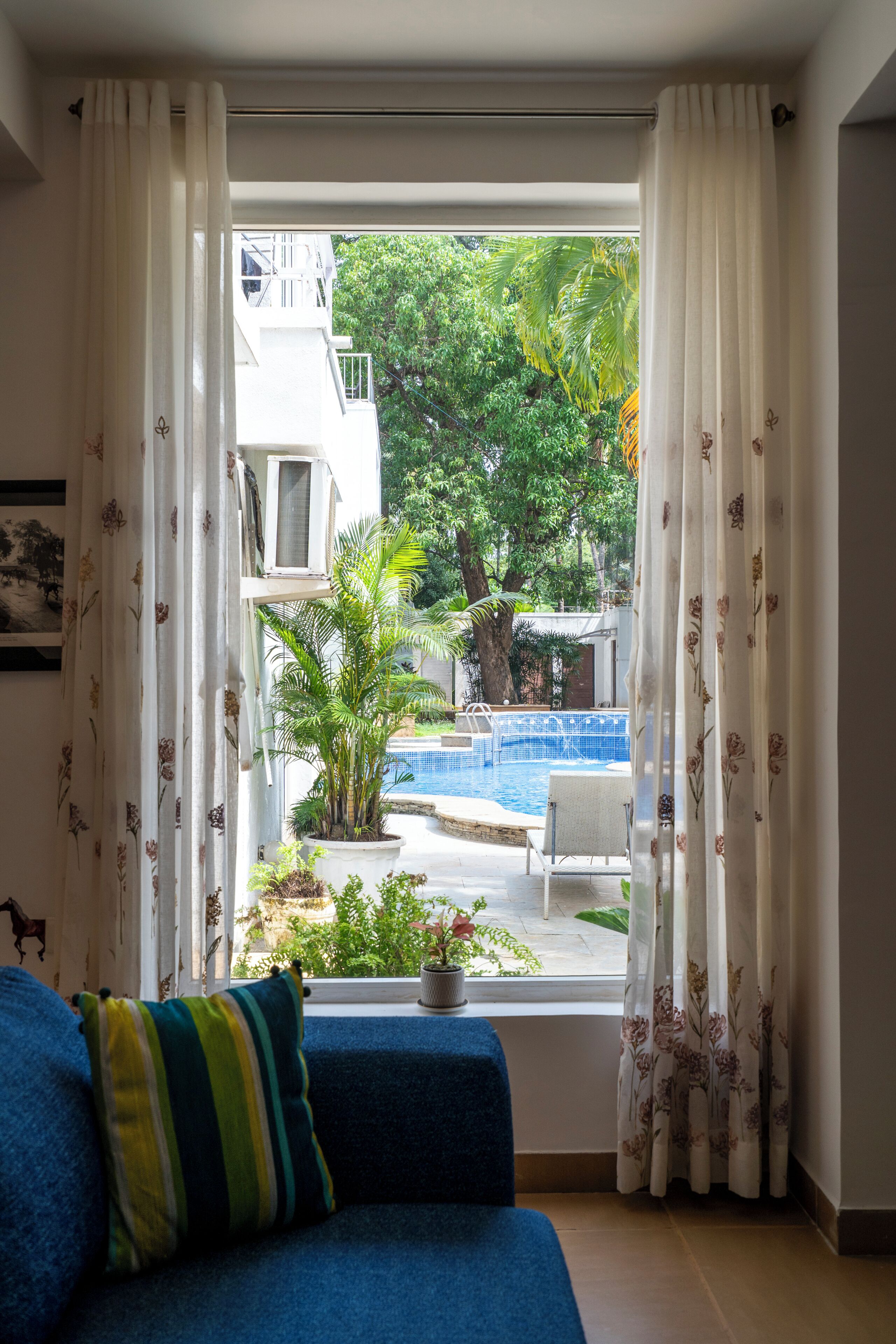 A room with a view of a swimming pool, a blue sofa, and a window with curtains.