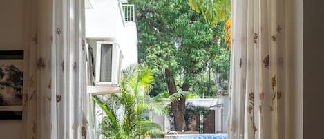 A room with a view of a swimming pool, a blue sofa, and a window with curtains.
