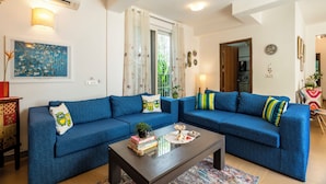 A living room with a blue sofa set, a coffee table with books and a decorative item, and a ceiling fan.