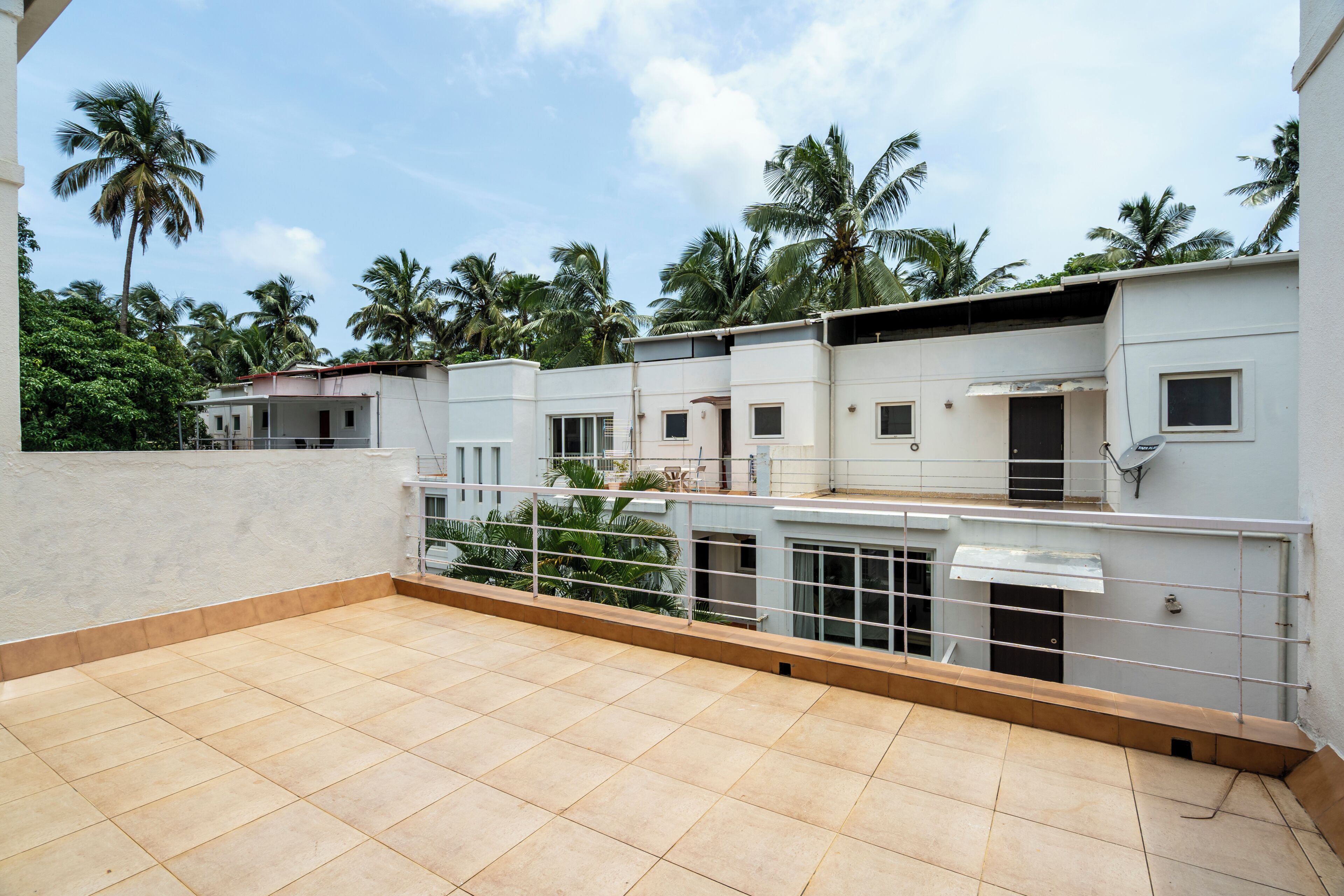 A residential building with multiple balconies, a tiled terrace, and palm trees in the background.
