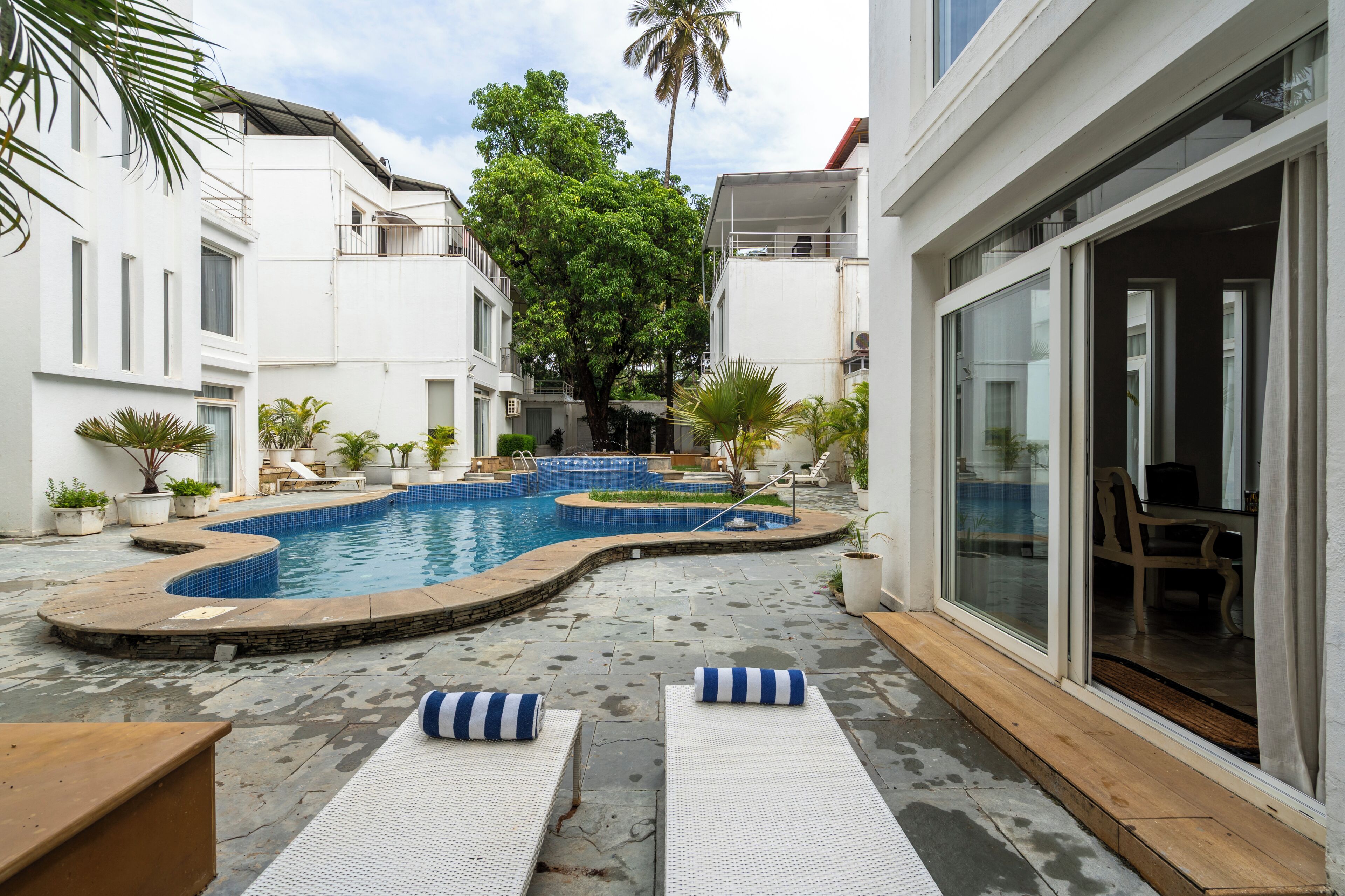 A swimming pool area with multiple pools, lounge chairs, and potted plants.