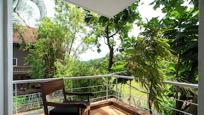 A balcony with a wooden chair, surrounded by lush greenery and a view of a residential area.
