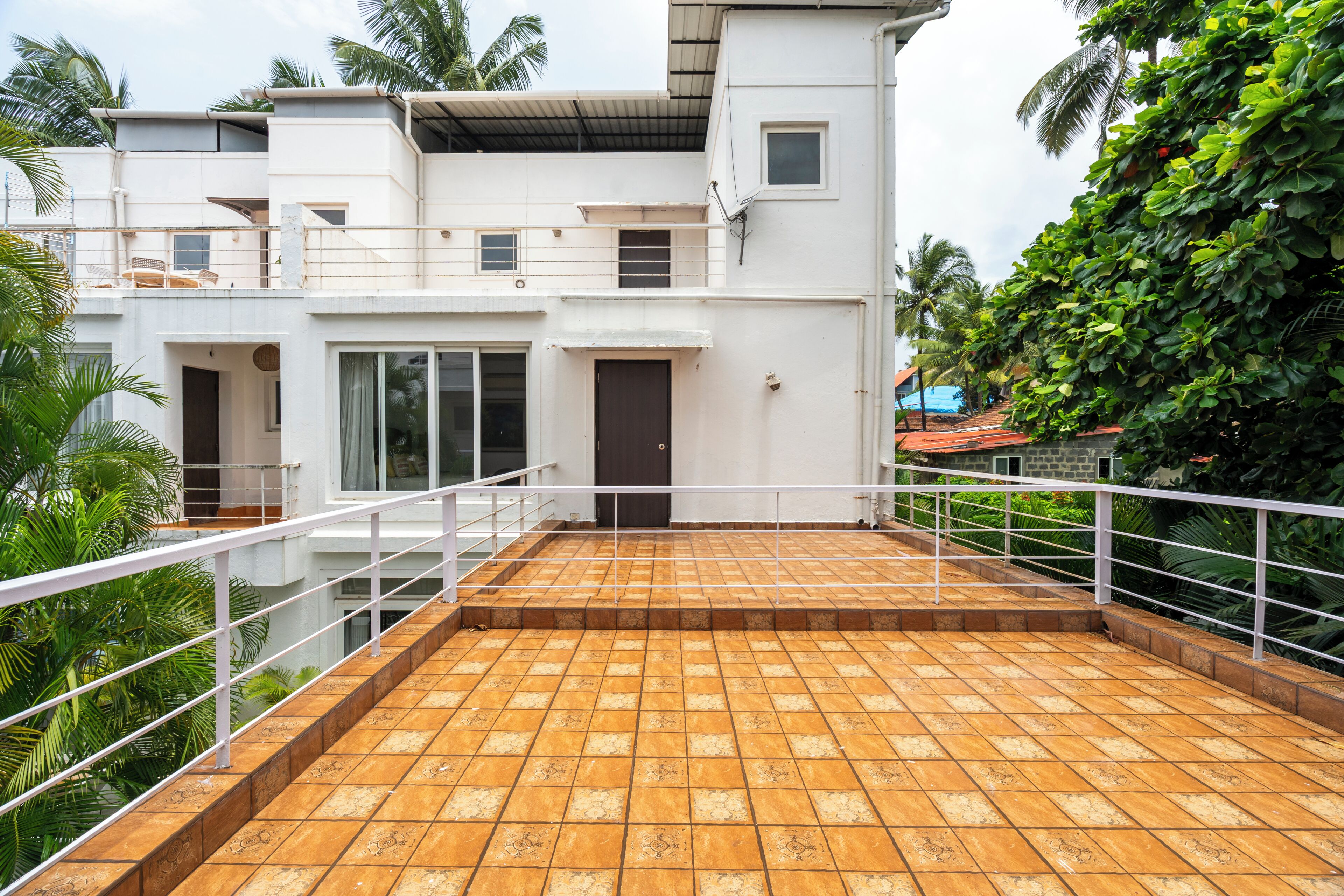 A multi-story building with a flat roof terrace, railings, and a view of lush greenery.