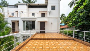 A multi-story building with a flat roof terrace, railings, and a view of lush greenery.