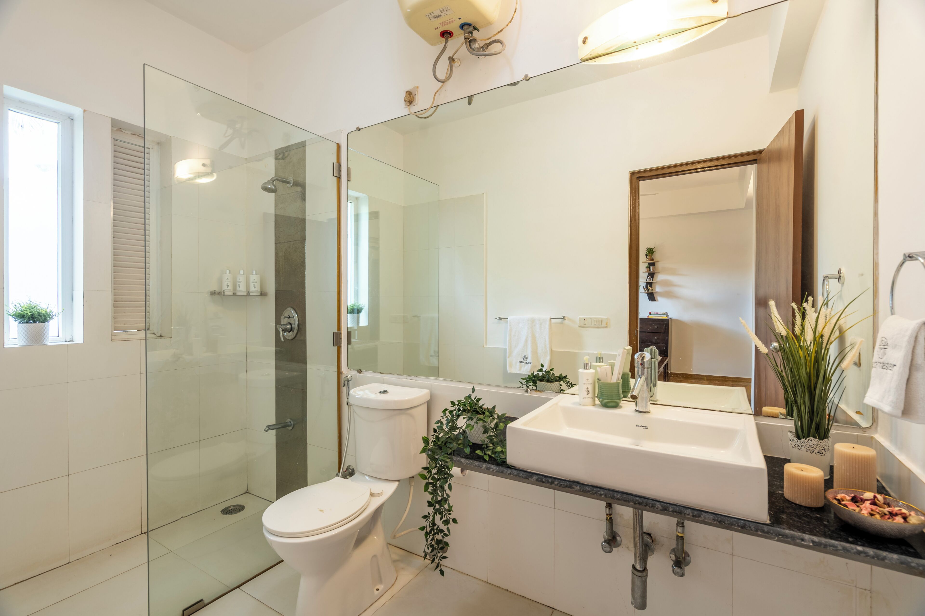 A modern bathroom with a glass shower enclosure, a white toilet, a large sink with a mirror, and a potted plant.