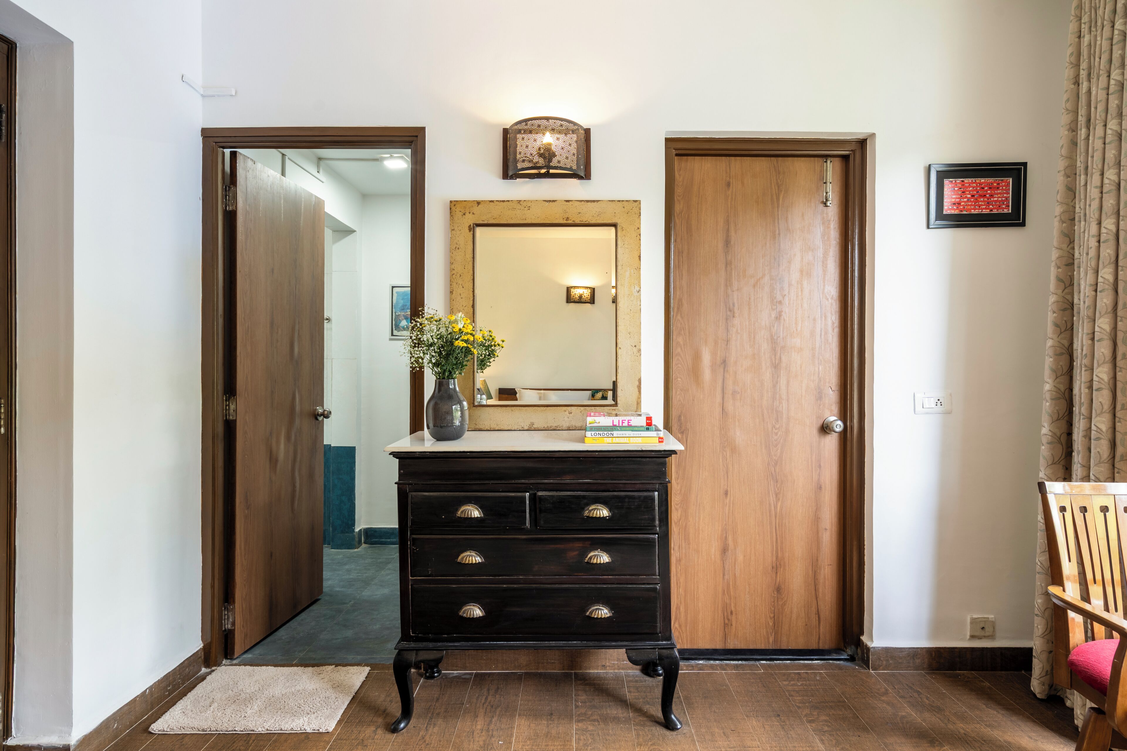 A hallway with a wooden door, a dresser with drawers, a mirror, and a vase with flowers.