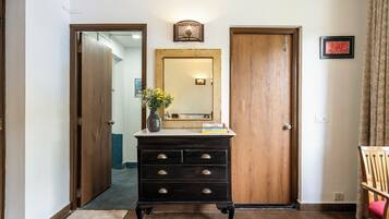 A hallway with a wooden door, a dresser with drawers, a mirror, and a vase with flowers.