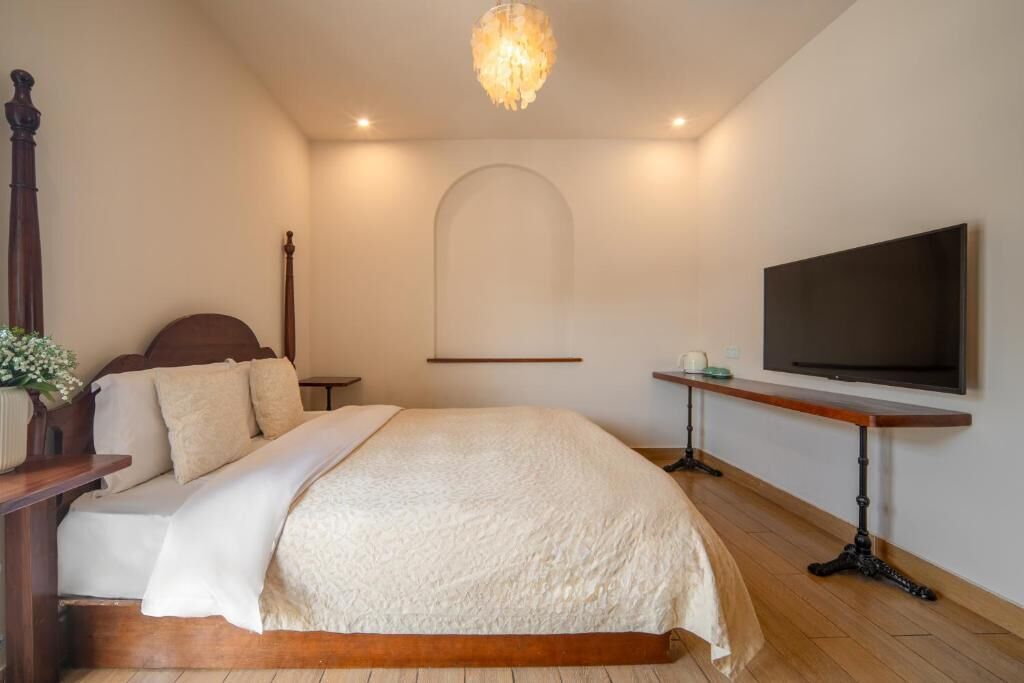 A bedroom with a bed, a television, a desk, and a chandelier.