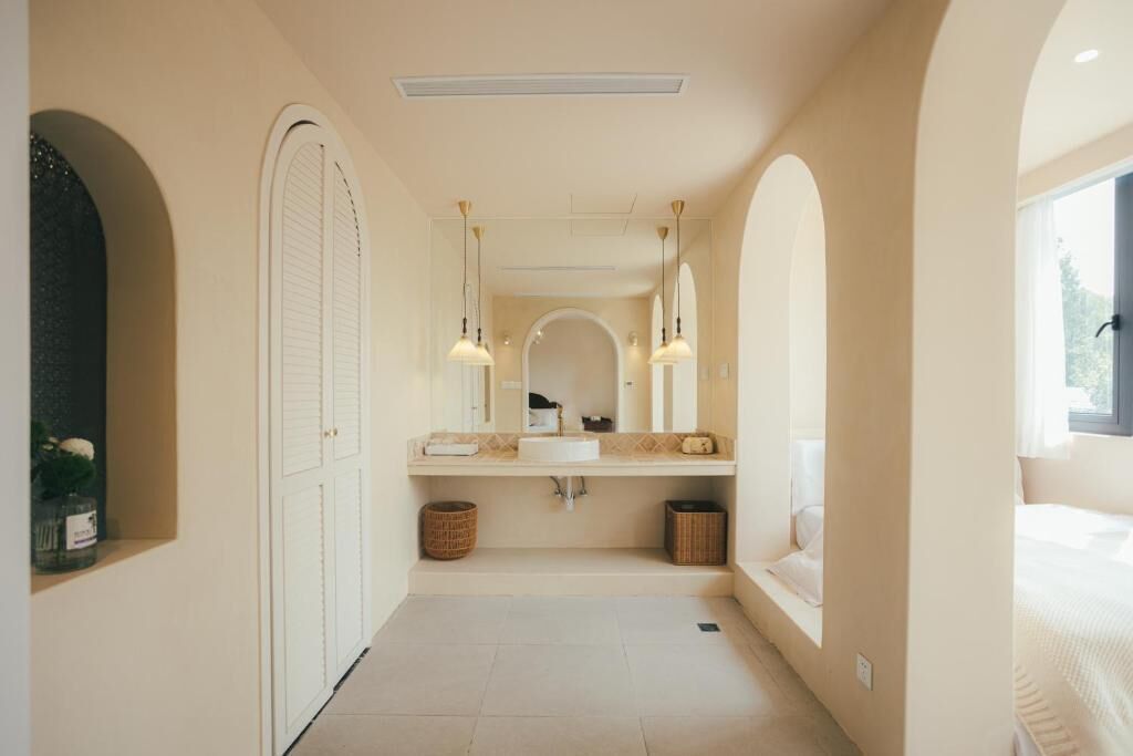 Un pasillo estrecho que conduce a un baño con un espejo grande, un lavamanos y una ventana.