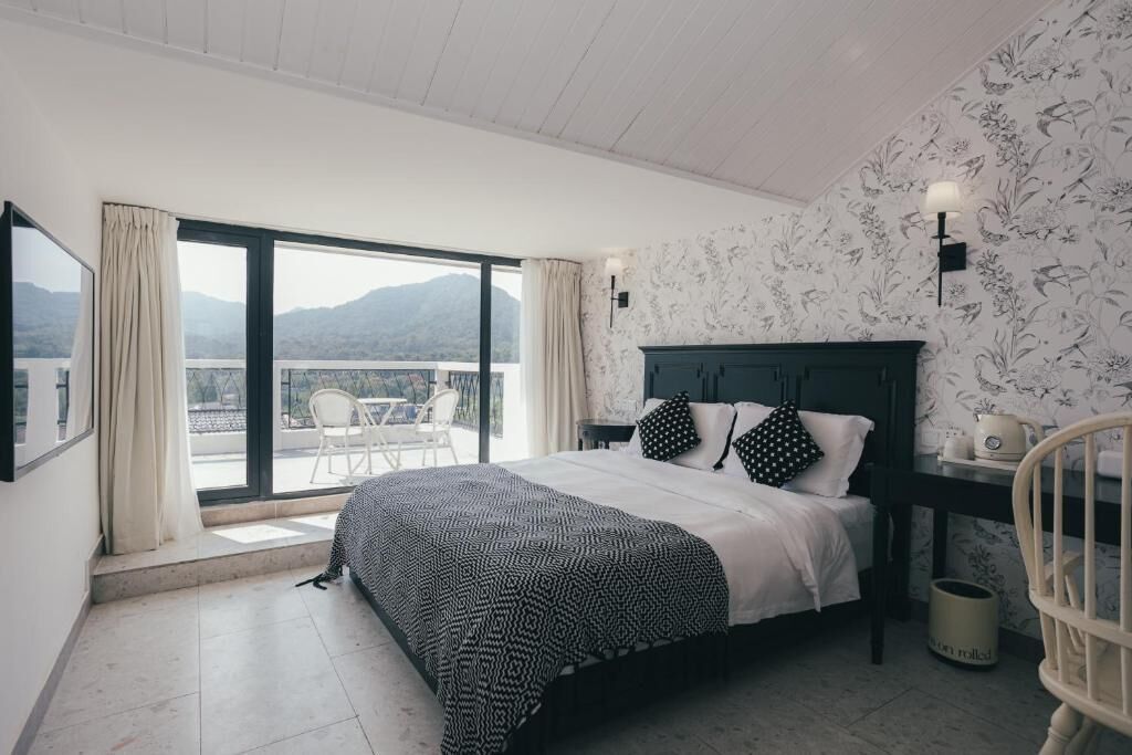 A bedroom with a bed, a nightstand, a chair, a window with curtains, and a view of the outdoors.