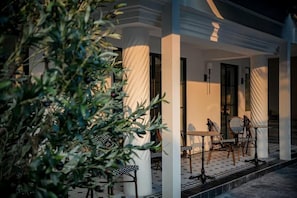 A covered outdoor seating area with chairs and tables, a column, and a potted plant.
