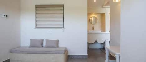 Un dormitorio con cama, un banco, una ventana con persianas, un espejo y un lavabo.