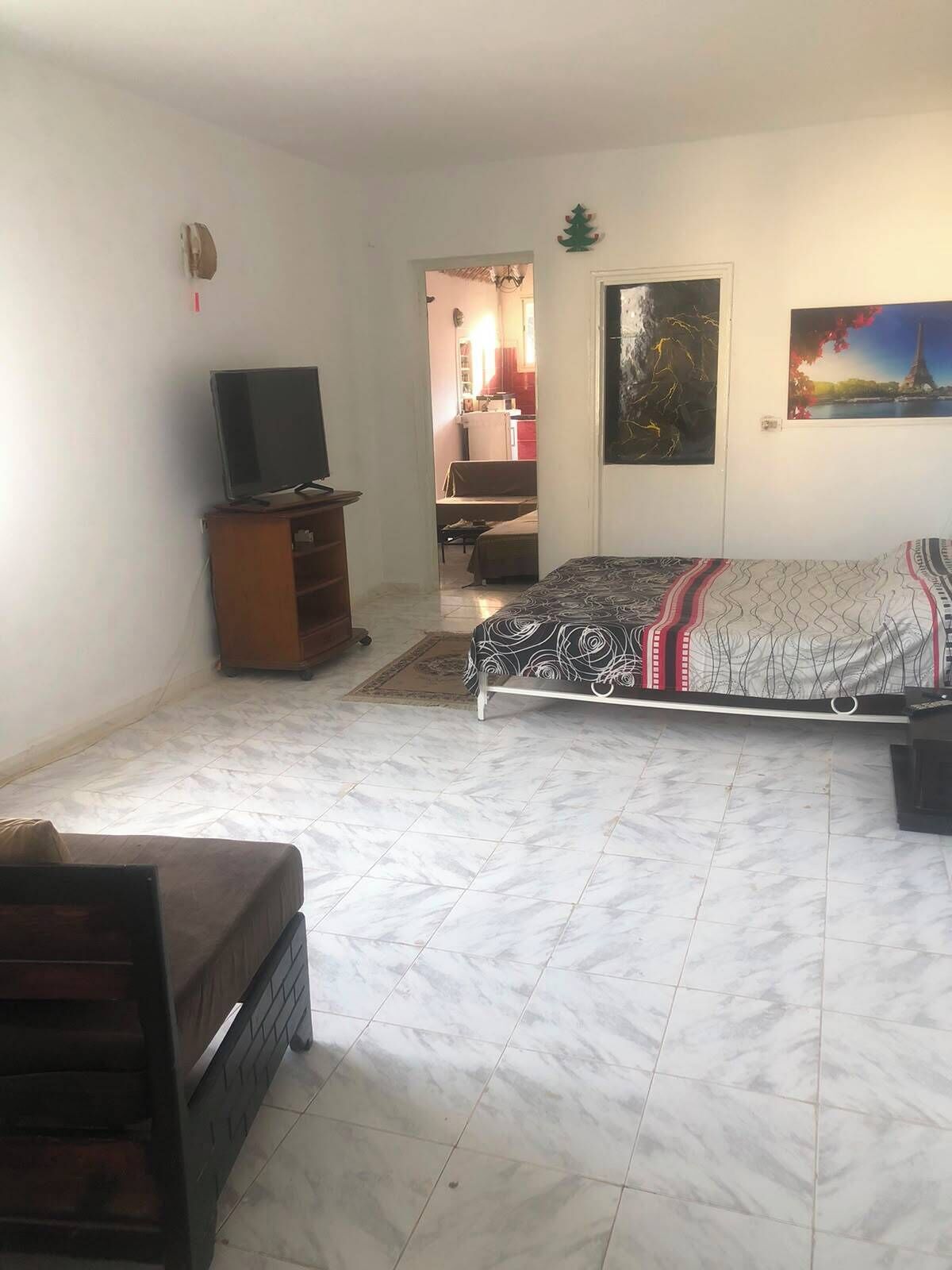 A bedroom with a bed, a television on a stand, a dresser, and a door leading to a bathroom.