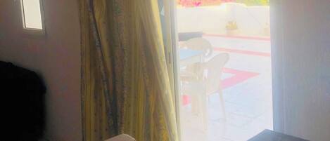 A room with a bed, a window with curtains, a door, and a wall-mounted picture.