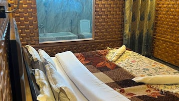 A hotel room with a large bed, a window with curtains, a wooden wall design, and a bathtub visible through the window.