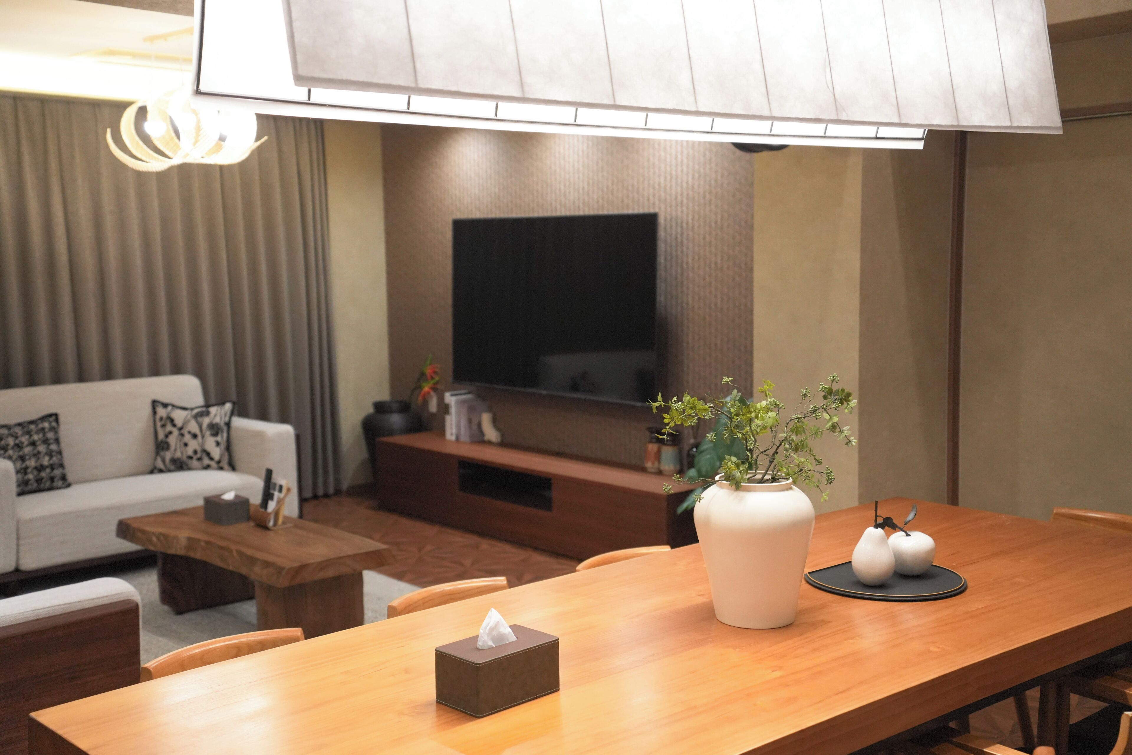 A modern living room with a sofa, coffee table, and a dining table with a vase and a tissue box.