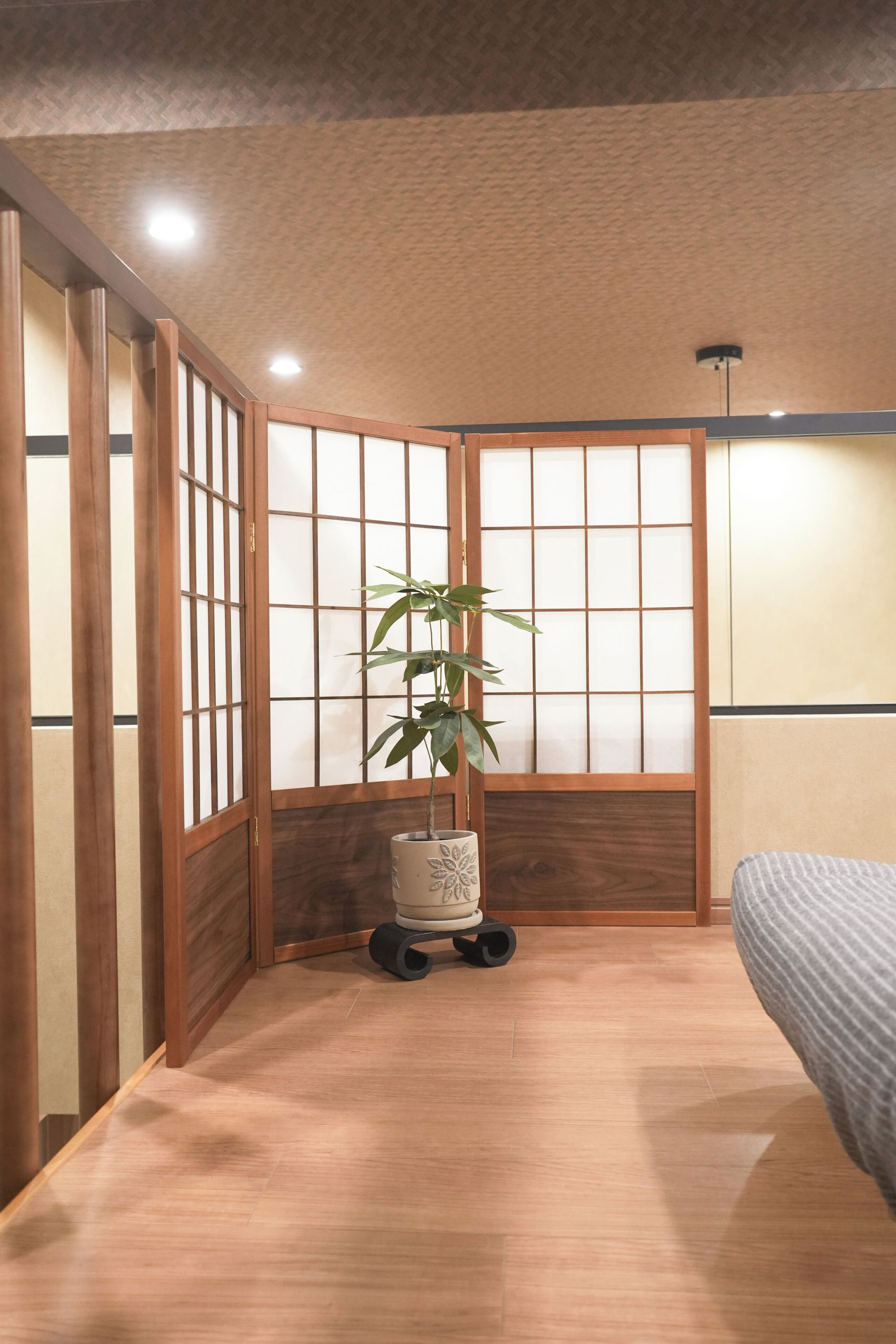 A traditional Japanese-style room with sliding doors, a bed, a plant, and a small table.