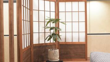 A traditional Japanese-style room with sliding doors, a bed, a plant, and a small table.