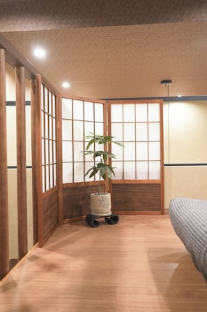 A traditional Japanese-style room with sliding doors, a bed, a plant, and a small table. - b&Kuromon 4 (Osaka)