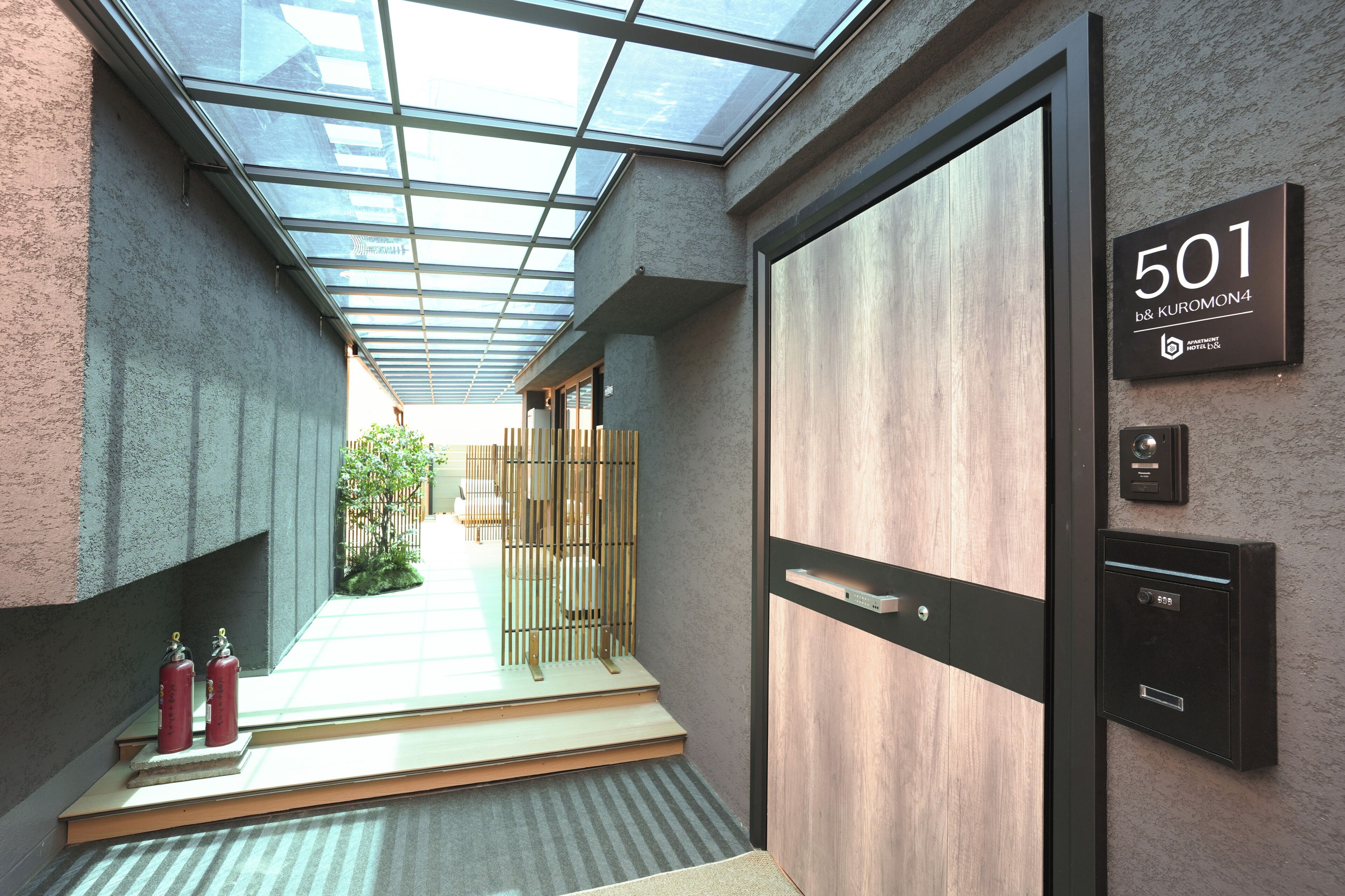 A modern hotel corridor with a glass ceiling, a wooden door labeled '501', and a fire extinguisher on the left.