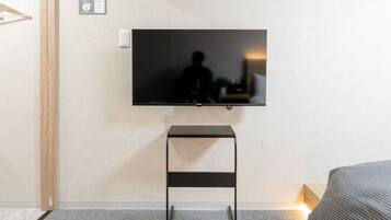 A modern bedroom with a flat-screen TV mounted on the wall, a wooden door, and a grey carpet.