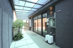 A modern building entrance with a glass door, a small outdoor seating area, and a fire alarm panel. - b&Kuromon 4 (Osaka)