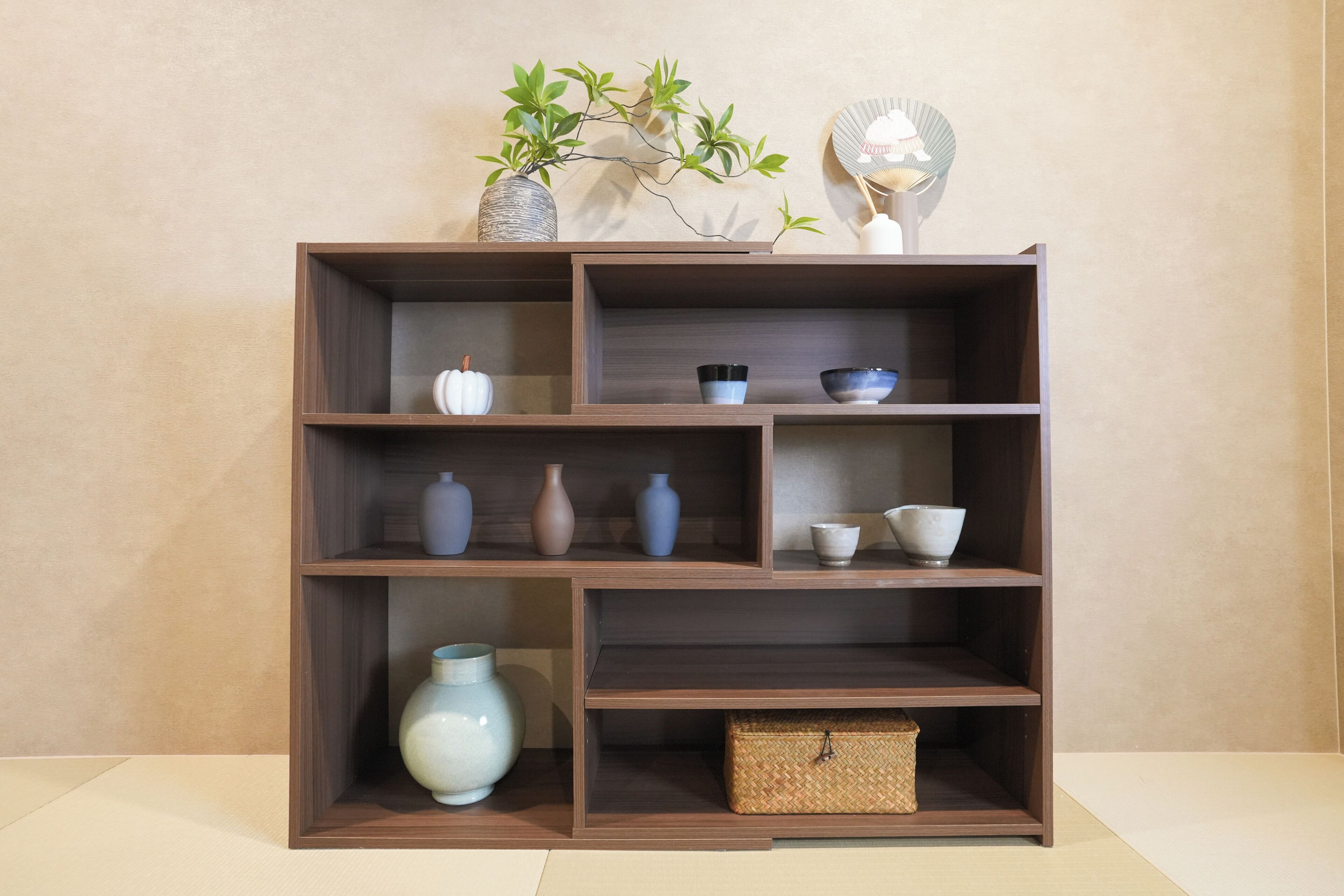 A wooden shelf unit with multiple compartments, some containing vases and bowls, and a small woven basket.