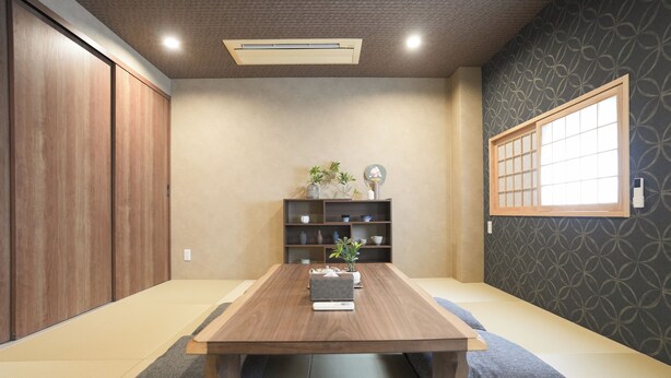 Una habitación con una mesa de madera, una estantería con adornos, una ventana con diseño de cuadrícula y un papel tapiz estampado.