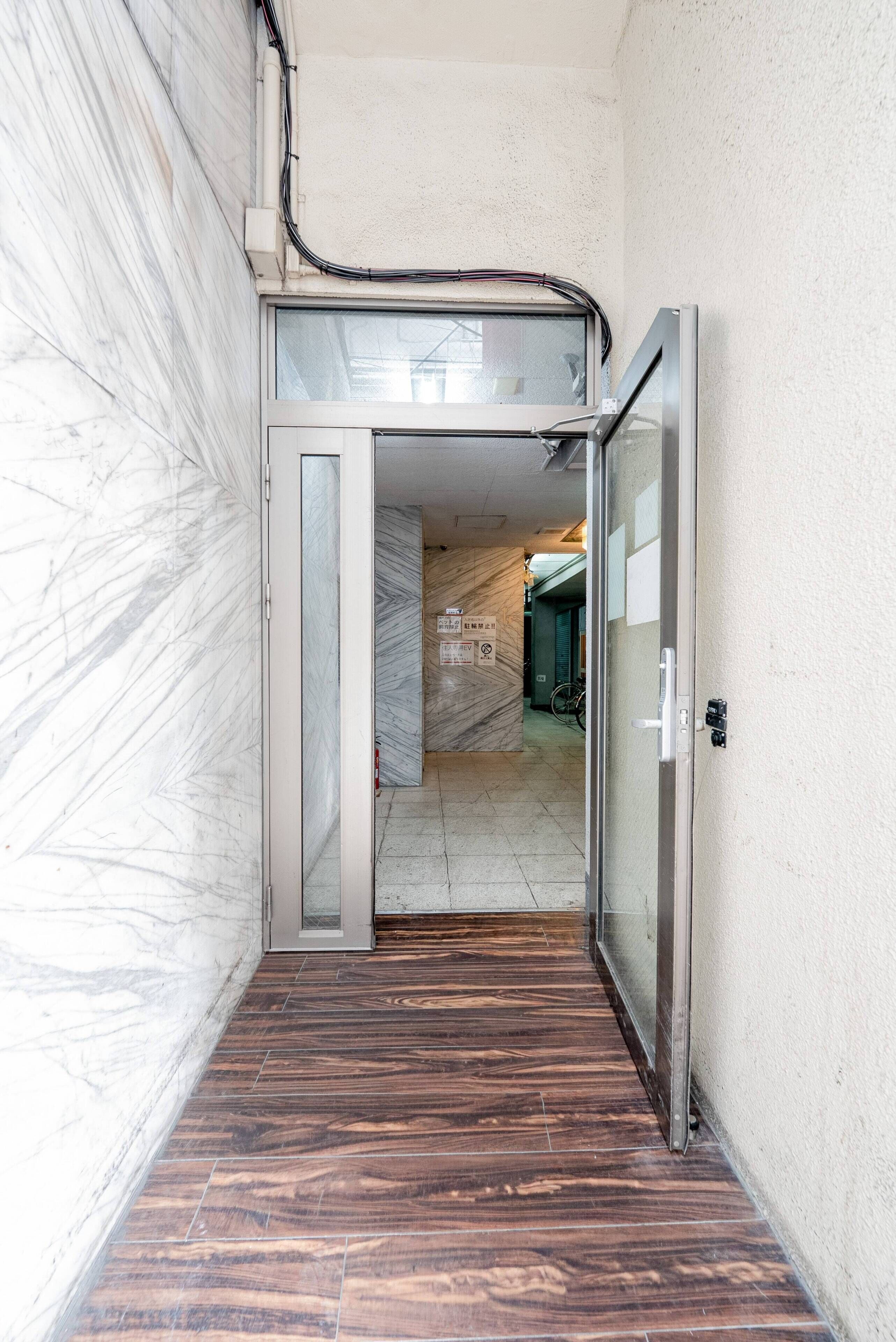 A narrow hallway with a glass door leading to a room with a tiled floor and a visible bicycle.