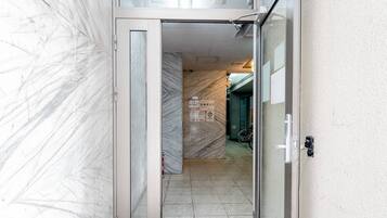 A narrow hallway with a glass door leading to a room with a tiled floor and a visible bicycle.