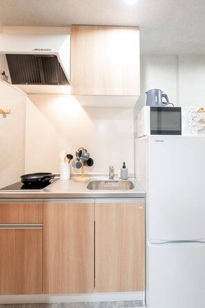 A compact kitchen with a microwave, stove, sink, and wooden cabinets. - b&Kuromon 4 (Osaka)