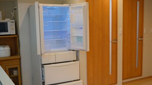 A white refrigerator with multiple shelves and a freezer compartment, positioned next to a wooden door and a microwave. - Glowlight 201 - 4-Bedroom Family Suite - 2-Minute Walk to Kuromon Market (Osaka)