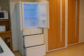 A white refrigerator with multiple shelves and a freezer compartment, positioned next to a wooden door and a microwave. - Glowlight 201 - 4-Bedroom Family Suite - 2-Minute Walk to Kuromon Market (Osaka)