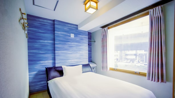 A hotel room with a bed, a nightstand, a window with curtains, and a wall with a blue textured design. - Glowlight 201 - 4-Bedroom Family Suite - 2-Minute Walk to Kuromon Market (Osaka)