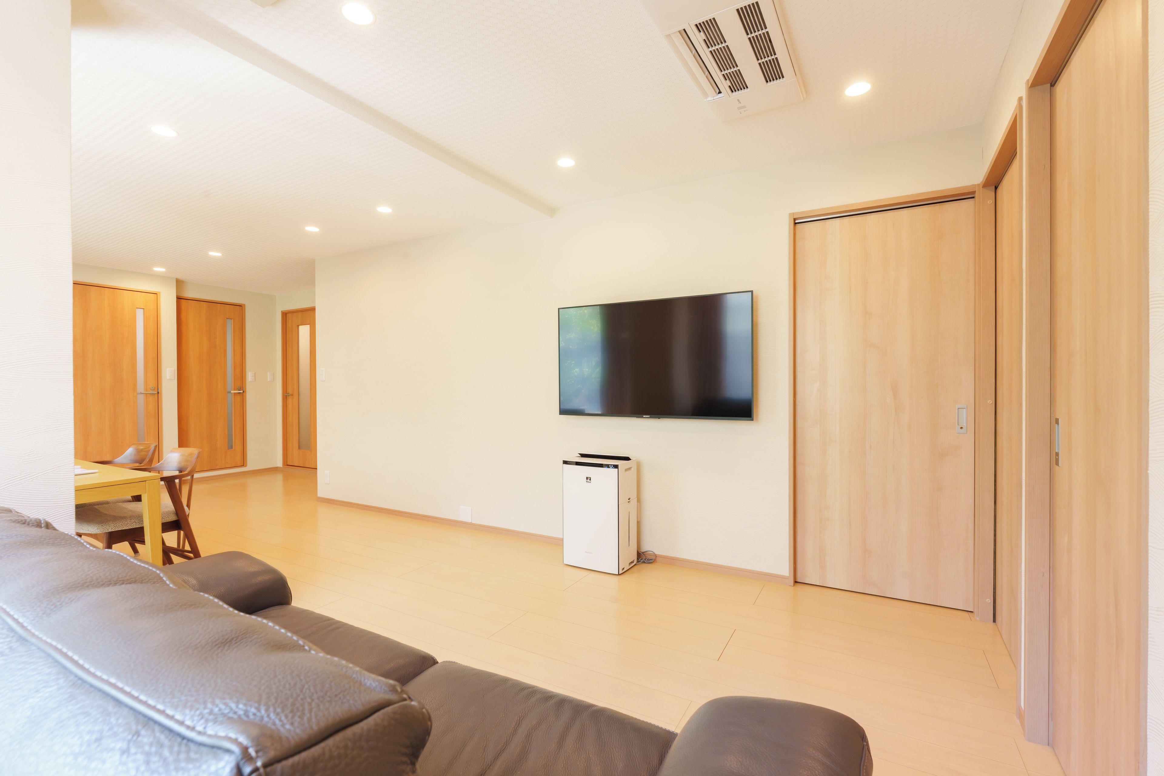 A modern living room with a flat-screen TV mounted on the wall, a white air conditioning unit, and a wooden wardrobe.