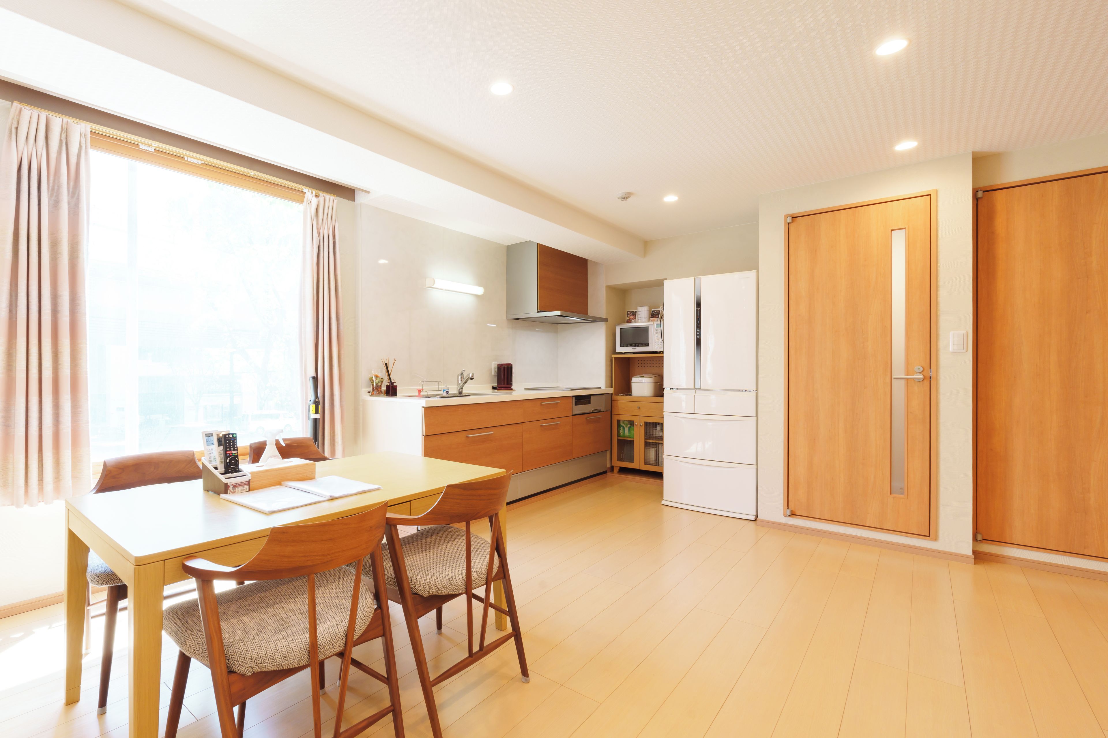 A modern kitchen with wooden cabinets, a dining table with chairs, and a large window with curtains.