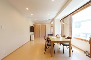 A spacious room with a wooden dining table, chairs, a television, and a large window. - SERENE | Kuromon ・ 201 | 4BR ・ 2 Shower Rooms | Private Home for Families and Groups (Osaka)