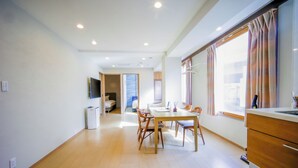 A spacious room with a dining area, a kitchenette, and a large window with curtains. - Glowlight 201 - 4-Bedroom Family Suite - 2-Minute Walk to Kuromon Market (Osaka)