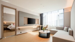 A modern hotel room with a large bed, a flat-screen TV mounted on the wall, a round coffee table, and a seating area with a sofa and armchairs. - Meilifeng Hotel  (Weihai)