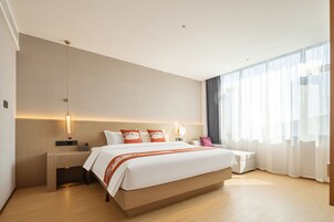 Una habitación de hotel moderna con una cama grande, mesitas de noche, un escritorio y una ventana con cortinas translúcidas.