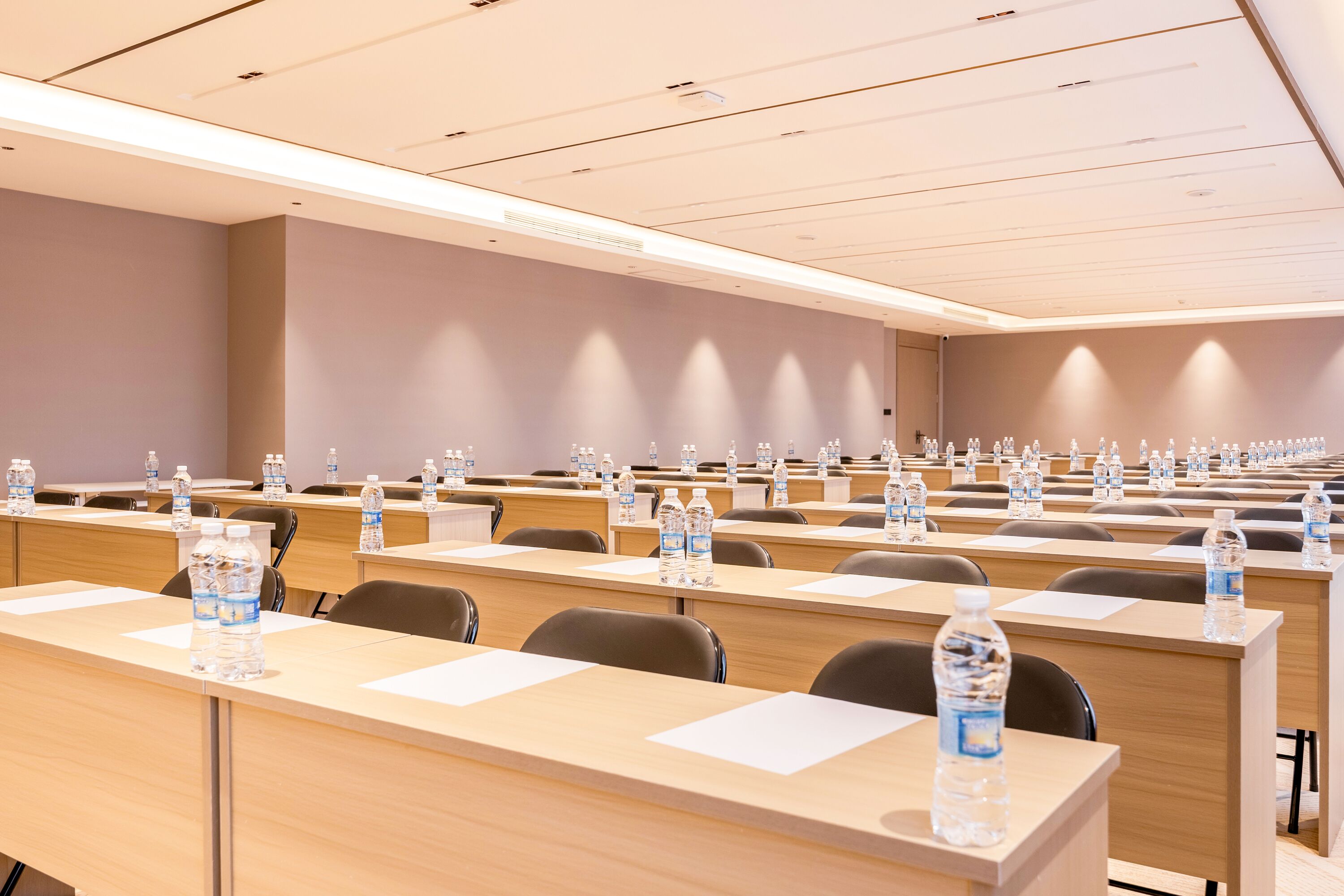 A conference room with rows of tables, each with a water bottle and a notepad.