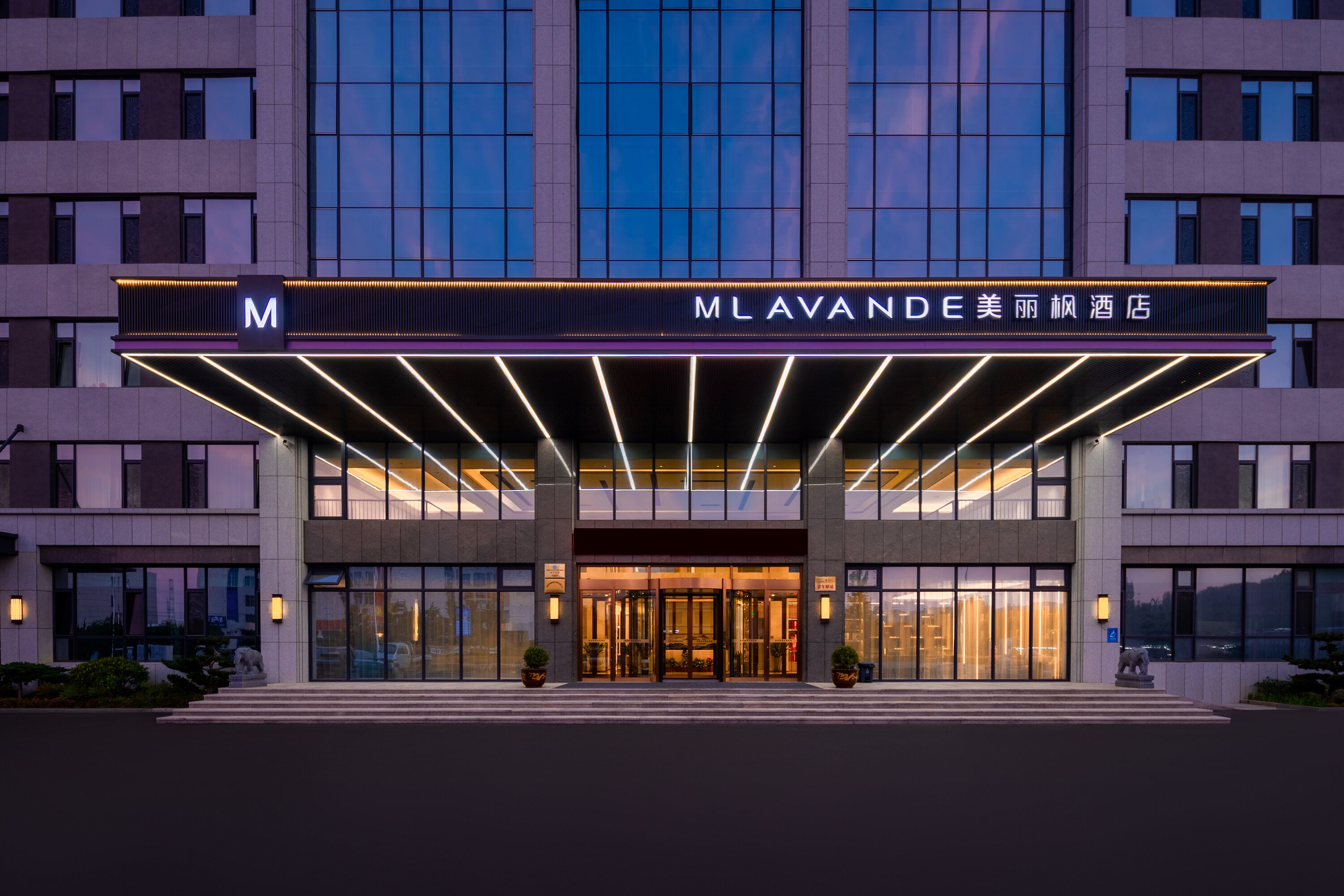 A hotel entrance with a modern design, featuring a prominent 'M' sign and illuminated signage.
