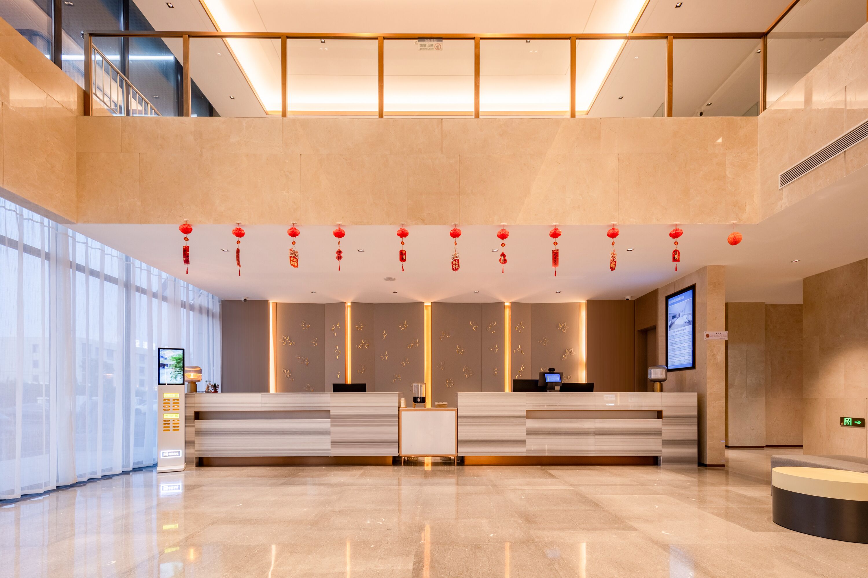 A modern hotel lobby with a reception desk, digital information display, and a high ceiling with decorative elements.