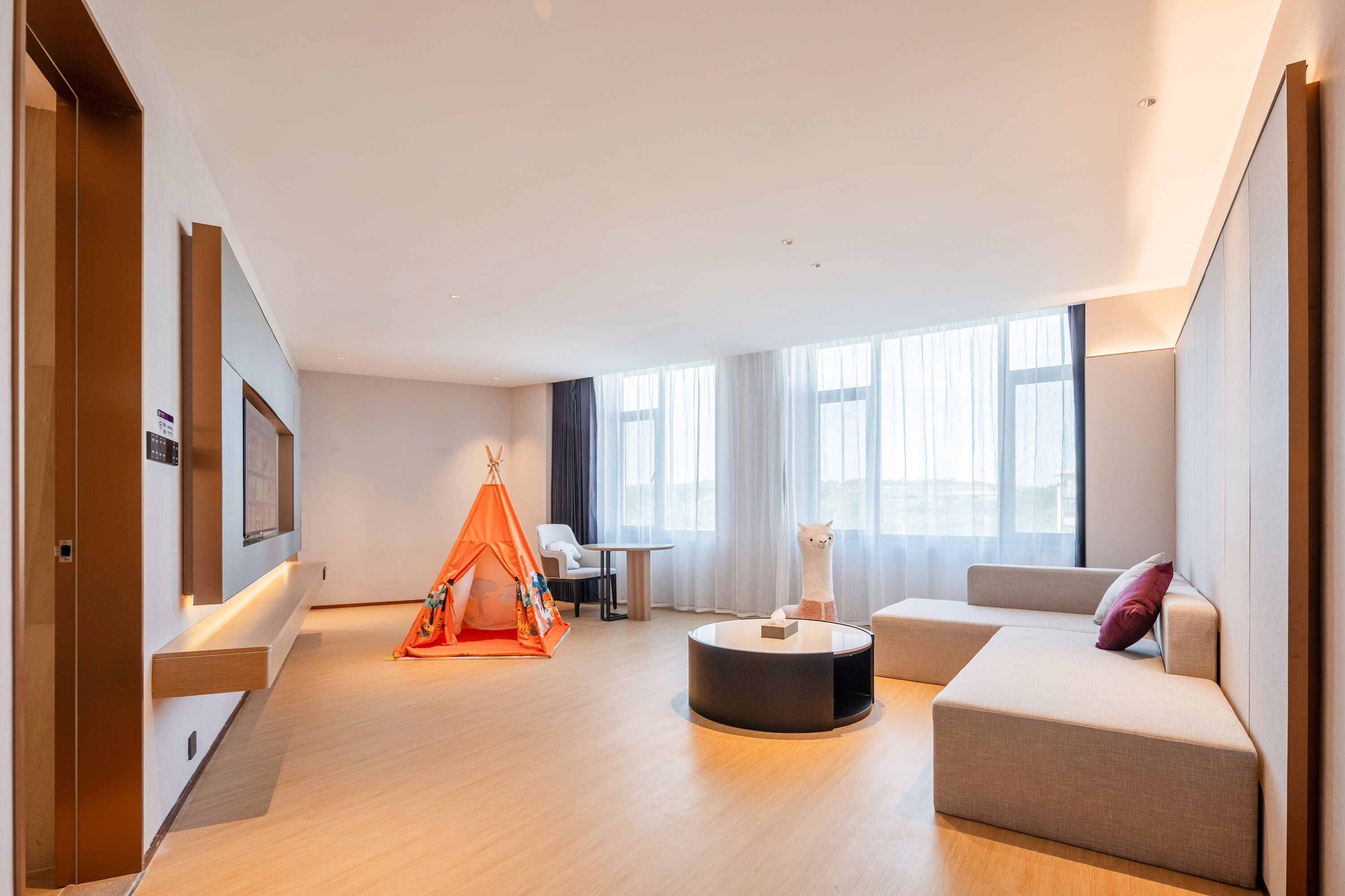 Ein modernes Wohnzimmer mit einer Couch, einem runden Couchtisch, einem Zelt und einem an der Wand befestigten Fernseher.
