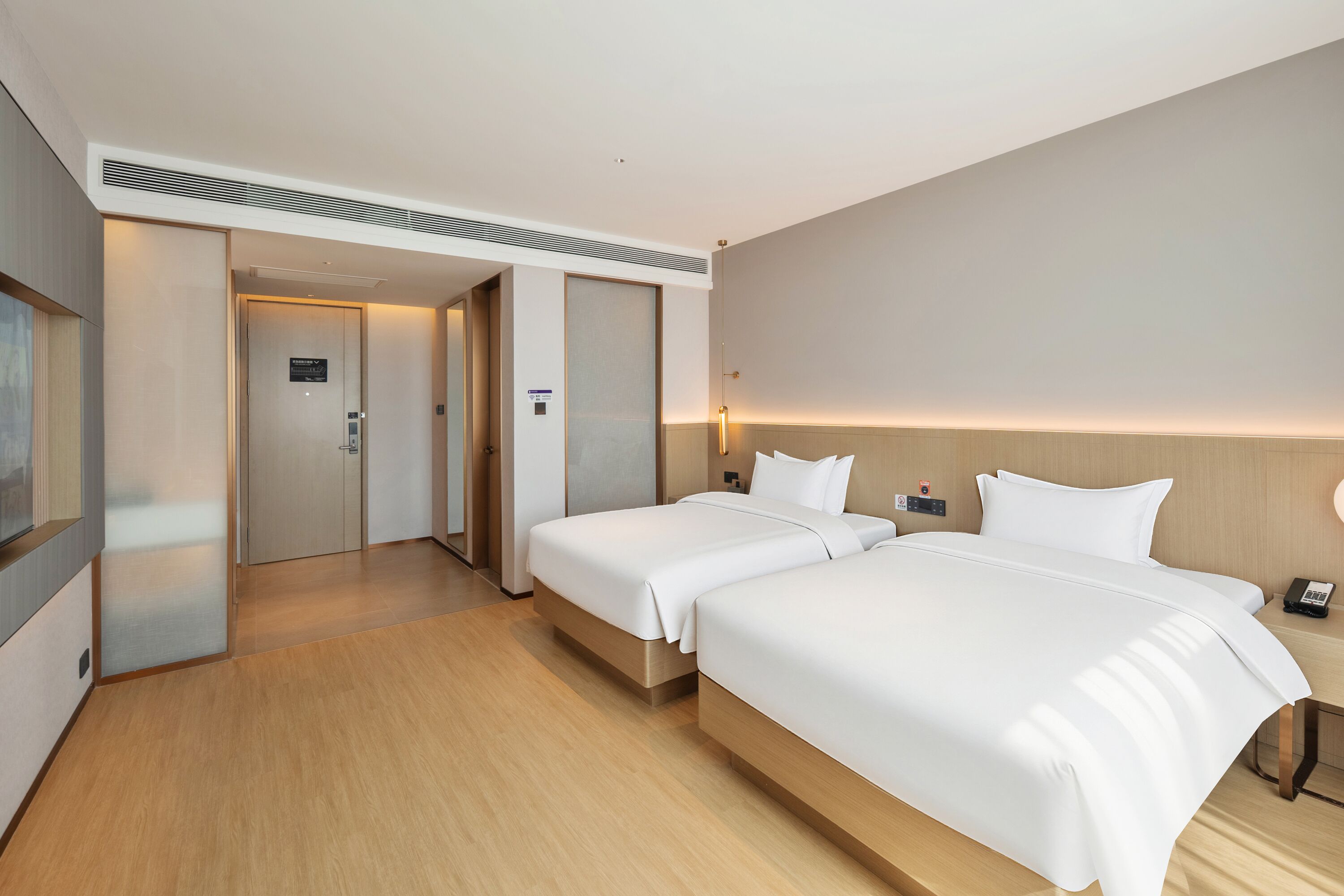 Habitación de hotel con dos camas, piso de madera, una puerta que da a un pasillo y un teléfono en la pared.