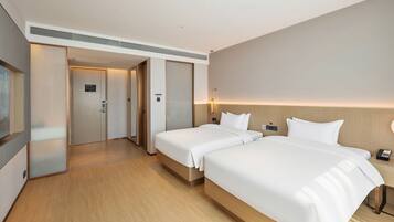 Habitación de hotel con dos camas, piso de madera, una puerta que da a un pasillo y un teléfono en la pared.