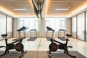 Un gimnasio con cintas de correr y bicicletas estáticas, ventanas amplias y un diseño de techo moderno.