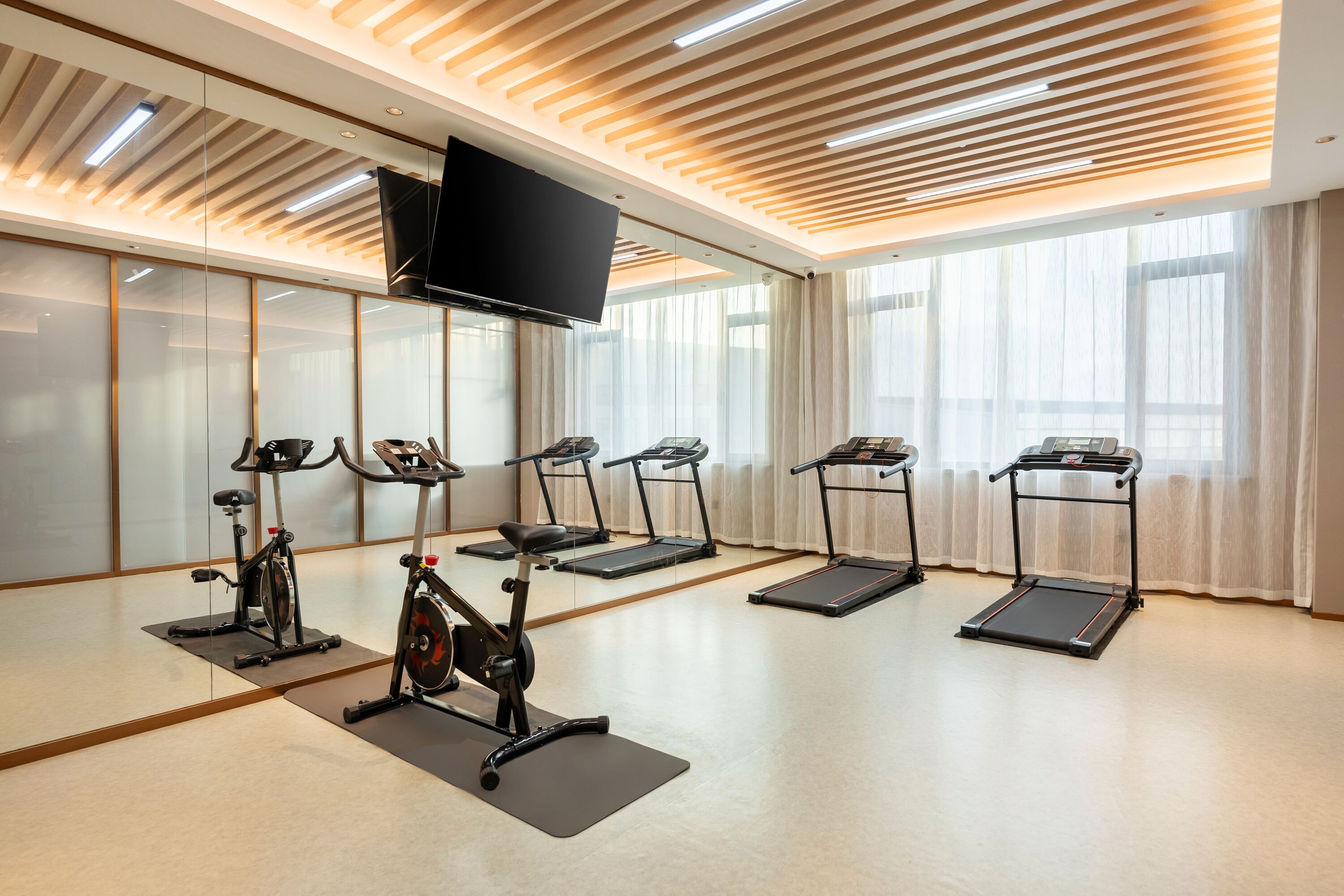 A fitness room with exercise equipment, a television, and large windows.