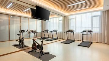 A fitness room with exercise equipment, a television, and large windows.