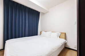 A single bed with a wooden headboard in a room with white walls and a dark blue curtain. - SERENE Osaka | 3 Minutes from Kuromon | 6F-603 | 35 ㎡, 2-Bedroom | Sleeps 4 (Osaka)